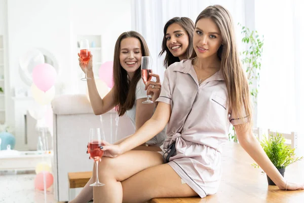 Pijama partisi. Çekici, pijamalı, gülümseyen kadınlar yatak odasında pijama partisi yaparken şampanya içiyorlar.. — Stok fotoğraf