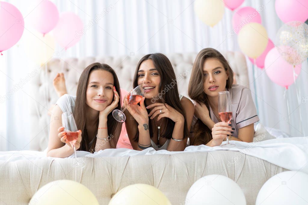 Pajama party. Attractive young smiling women in pajamas drinking champagne while having a slumber party in the bedroom.