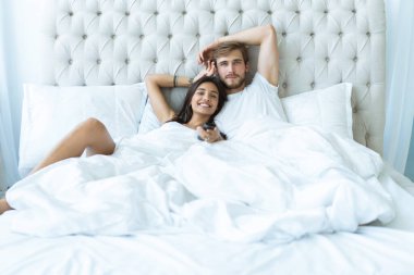 Uzaktan kumandalı mutlu çift evde yatıp televizyon izliyor..