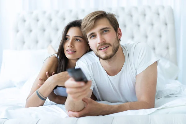 Feliz pareja con remoto acostado en la cama en casa y viendo la televisión . — Foto de Stock