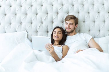 mutlu genç bir çift yatak odası yatakta yatan ve dijital tablet kullanma.