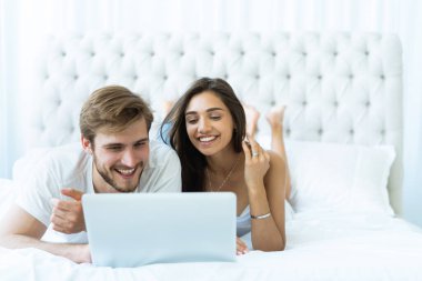 Dizüstü bilgisayarlı genç çift odadaki yatakta..