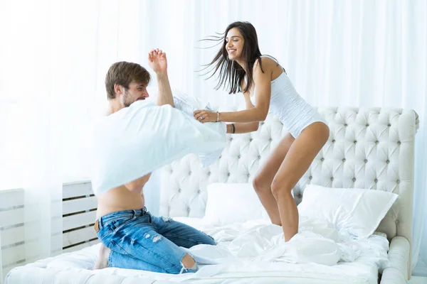 La joven pareja feliz se divierte en la cama. Disfrutando de la compañía del otro. Batalla de almohadas . —  Fotos de Stock