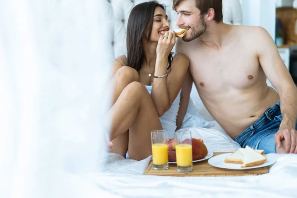 Desayuno saludable en la cama. Joven hermosa pareja de amor está sentado en la cama antes de desayunar . — Foto de Stock