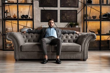 Havalı ve yakışıklı. Takım elbiseli yakışıklı genç adam kanepede oturuyor ve içeride vakit geçiriyor..