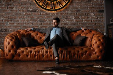 Havalı ve yakışıklı. Takım elbiseli yakışıklı genç adam kanepede oturuyor ve içeride vakit geçiriyor..