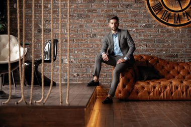 Havalı ve yakışıklı. Takım elbiseli yakışıklı genç adam kanepede oturuyor ve içeride vakit geçiriyor..