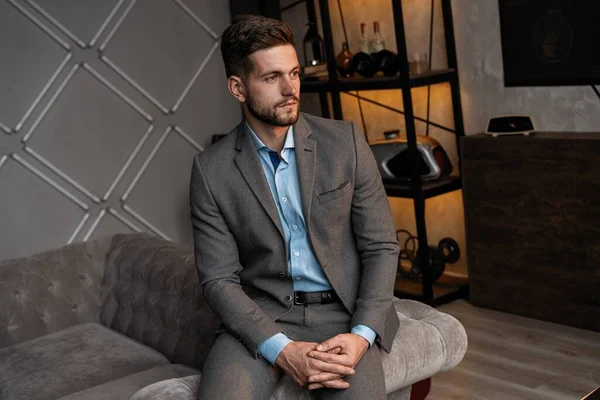 Cool and handsome. Good looking young man in full suit sitting on the sofa while spending time indoors. — Stock Photo, Image