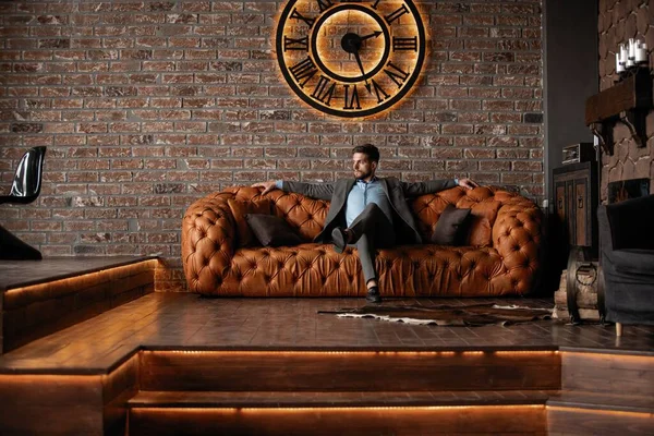 Cool and handsome. Good looking young man in full suit sitting on the sofa while spending time indoors. — Stock Photo, Image