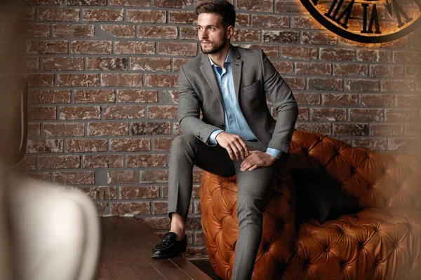 Cool and handsome. Good looking young man in full suit sitting on the sofa while spending time indoors. — Stock Photo, Image