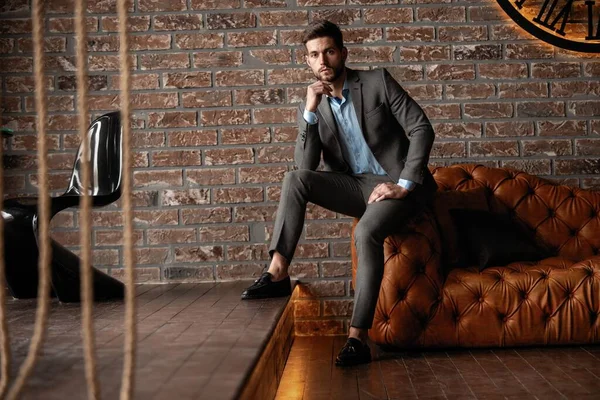 Cool and handsome. Good looking young man in full suit sitting on the sofa while spending time indoors. — Stock Photo, Image