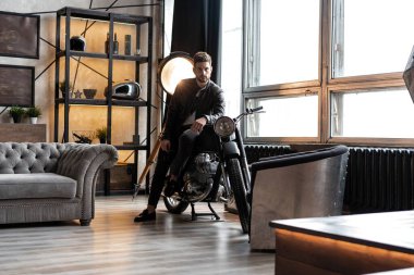 Deri ceketli şık genç adam motosiklette oturuyor..