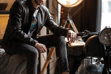 Deri ceketli yakışıklı genç adam taburede otururken gözlerini kaçırıyor.