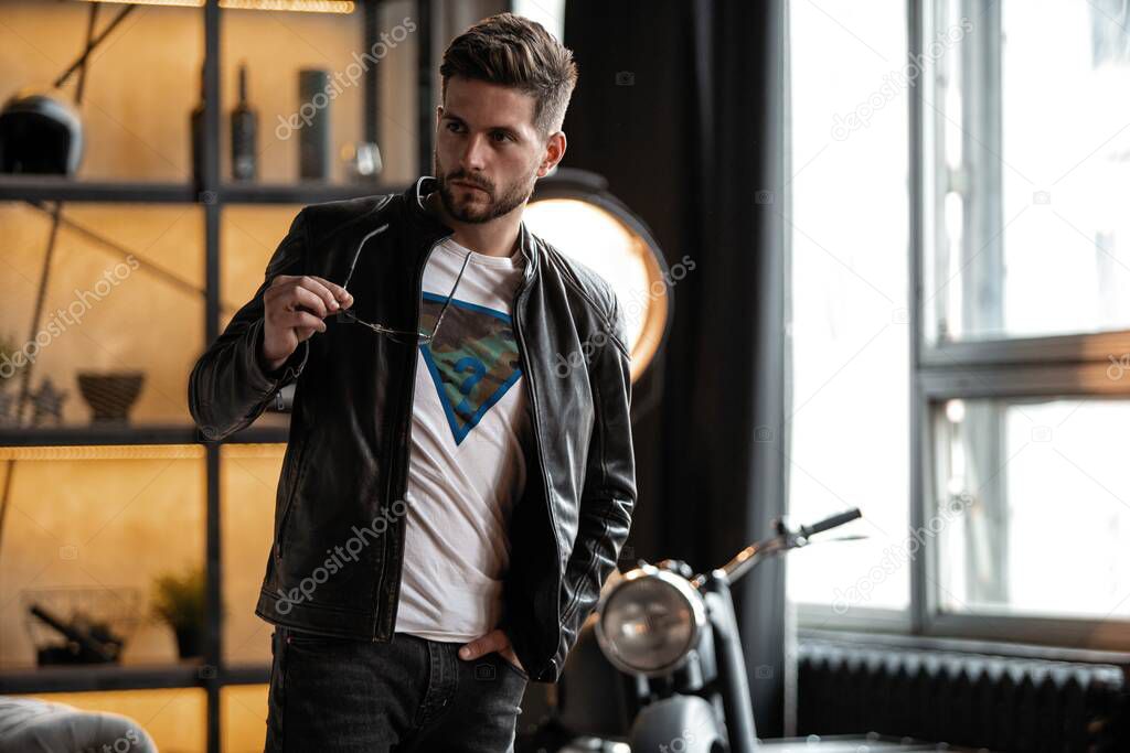 Perfect man. Young hipster in leather jacket standing in room.