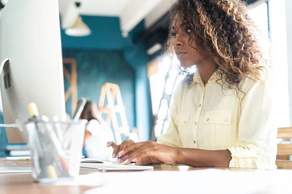 Joven mujer de negocios afroamericana sentada en la oficina y trabajando en la computadora portátil . — Foto de Stock