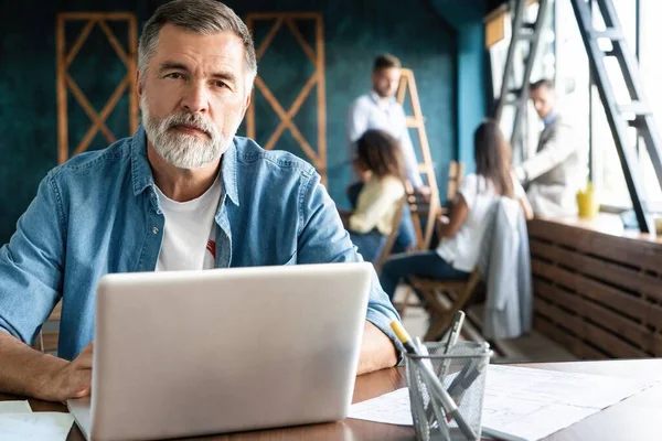 Vrolijke volwassen man werken op laptop en glimlachen terwijl zitten op zijn werkplek — Stockfoto