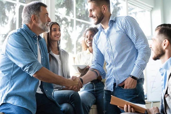 Los hombres de negocios en ropa casual inteligente estrechando las manos mientras trabajan en la oficina creativa . — Foto de Stock