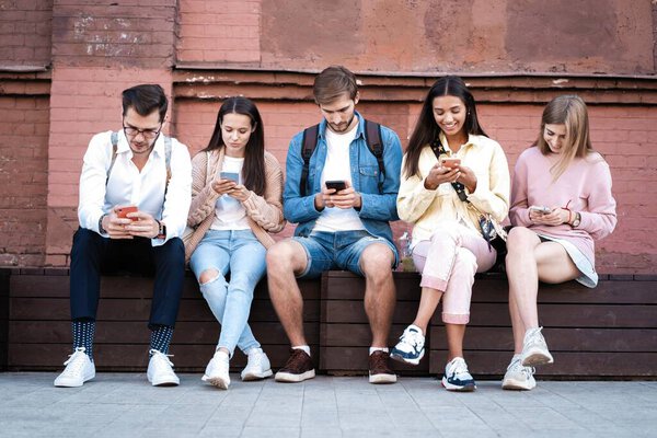 Modern Generation. Group of young people using gadgets, sitting on stairs outdoor, free space