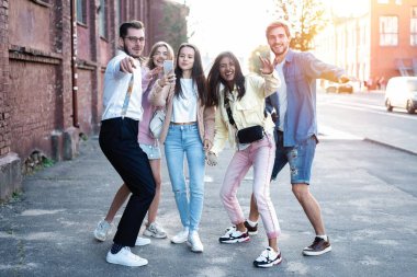 Mutlu arkadaşlar şehir merkezindeki açık havada yürürken eğleniyor - genç milenyum insanları birlikte dans ediyor