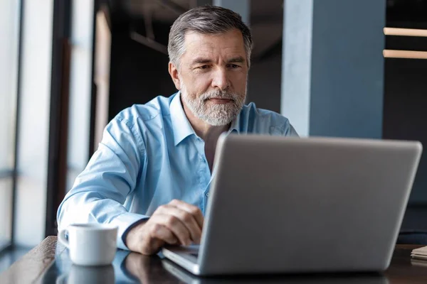 Gammal affärsman som jobbar på laptop. Snygg mogen företagsledare som sitter på ett modernt kontor — Stockfoto