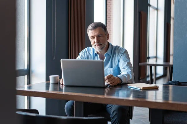 Volwassen zakenman werkt aan een laptop. Knappe volwassen business leader zittend in een modern kantoor — Stockfoto