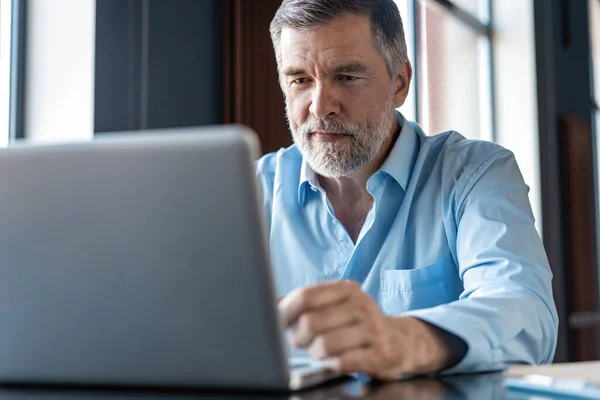 Volwassen zakenman werkt aan een laptop. Knappe volwassen business leader zittend in een modern kantoor — Stockfoto