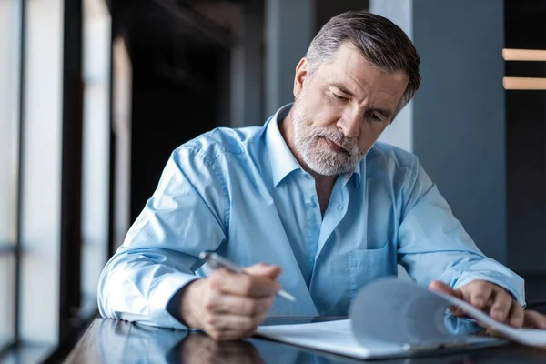 Empresario sentado en un restaurante del centro de negocios, mirando a través del contrato . — Foto de Stock