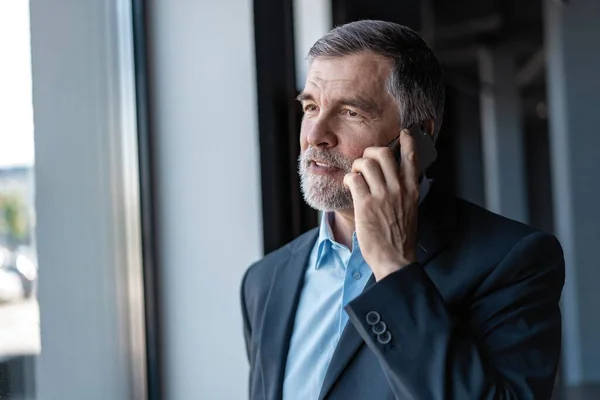 Homem de negócios sênior falar no telefone móvel no interior moderno escritório brilhante . — Fotografia de Stock