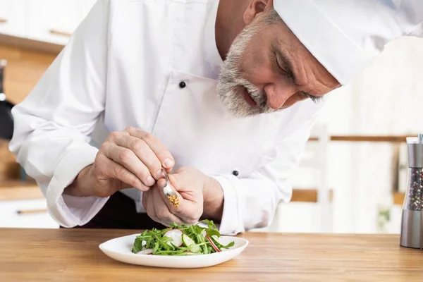 Повар-мужчина украшает гарниром приготовленное салатное блюдо на тарелке в ресторане коммерческой кухни . — стоковое фото