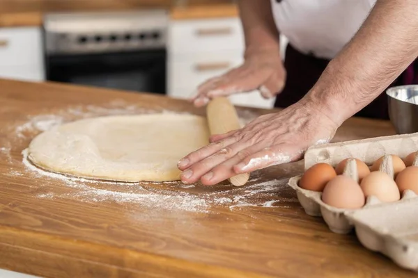 Homem fazendo padaria na cozinha e massa rolante na placa de corte de madeira coberta com farinha . — Fotografia de Stock
