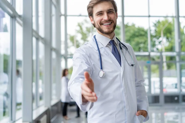 Junger Arzt bei der Begrüßung in seinem Büro. Arzt Mann lächeln, Hand Willkommensgeste mit Stethoskop. — Stockfoto