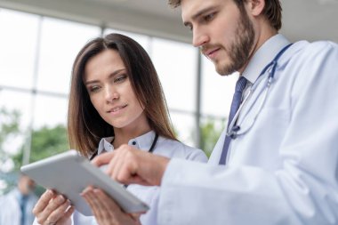 Kadın meslektaşıyla birlikte dijital tablet kullanan erkek doktor, birlikte çalışıyor..