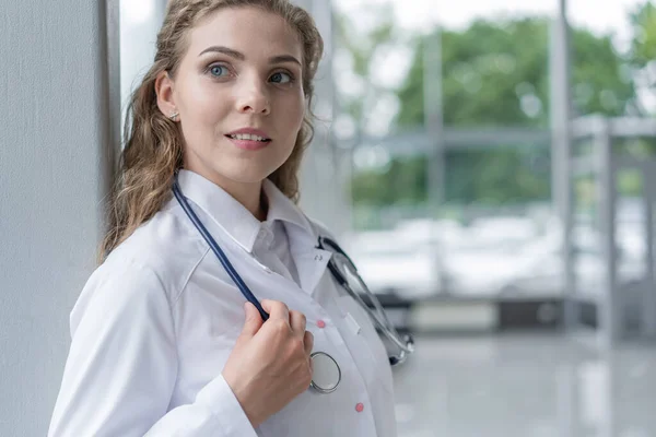 하얀 코트를 입고 병원에 서 있는 젊은 여자 의사의 모습. — 스톡 사진