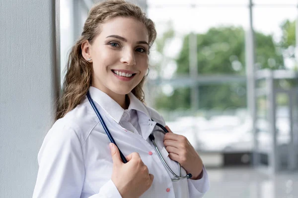 Προσωπογραφία νεαρής γυναίκας γιατρού με λευκό παλτό που στέκεται στο νοσοκομείο. — Φωτογραφία Αρχείου