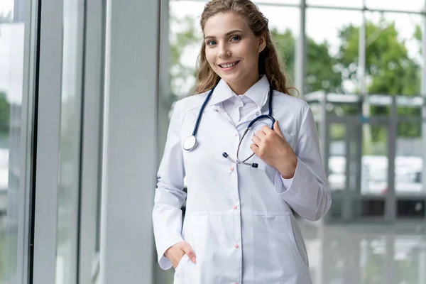 Retrato de una joven doctora con una bata blanca de pie en el hospital. — Foto de Stock