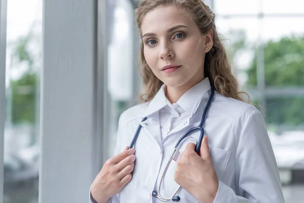 Retrato de una joven doctora con una bata blanca de pie en el hospital. — Foto de Stock