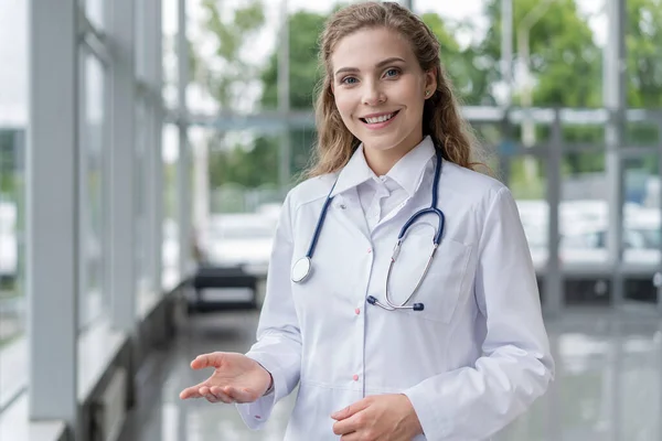 Portret van een jonge vrouwelijke arts met witte jas in het ziekenhuis. — Stockfoto