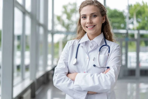 Προσωπογραφία νεαρής γυναίκας γιατρού με λευκό παλτό που στέκεται στο νοσοκομείο. — Φωτογραφία Αρχείου