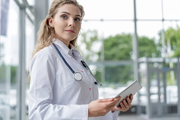 Conceito de saúde, tecnologia e medicina - médico sorridente feminino com estetoscópio tomar notas no computador tablet pc . — Fotografia de Stock