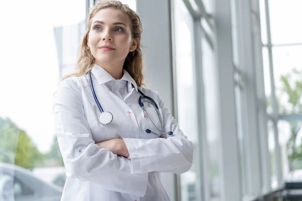 Retrato de una joven doctora con una bata blanca de pie en el hospital. — Foto de Stock