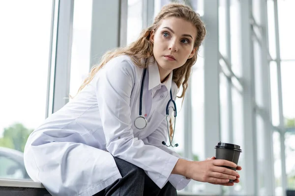 Porträt einer müden, erschöpften Krankenschwester oder Ärztin, die im Krankenhaus eine Kaffeepause einlegt. COVID-19, Coronavirus-Pandemie. — Stockfoto