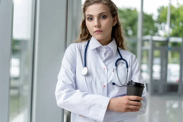 Porträt einer müden, erschöpften Krankenschwester oder Ärztin, die im Krankenhaus eine Kaffeepause einlegt. COVID-19, Coronavirus-Pandemie. — Stockfoto