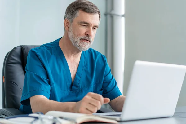 다 자란 남자 의사가 노트북 컴퓨터를 사용하며 의료 실에 앉아 있는 모습. — 스톡 사진