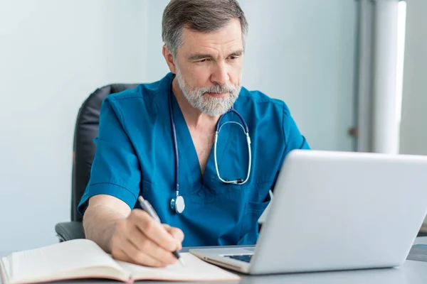 Felnőtt férfi orvos dolgozik laptop számítógép, ül az orvosi rendelőben. — Stock Fotó