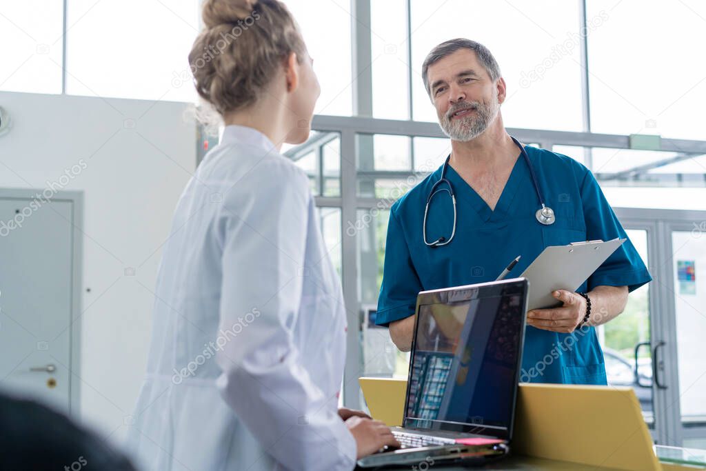 Doctor In Discussion With Nurse At Nurses Station or Hospital Reception.