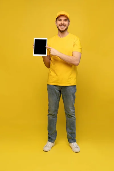 Cool bezorger met tablet. toont tablet. Ik kijk naar de camera. geïsoleerd op gele achtergrond. — Stockfoto