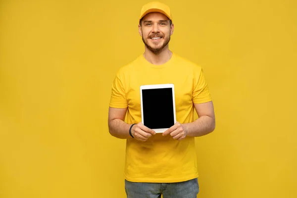 Cooler Zusteller mit Tablet. demonstriert Tablette. Blick in die Kamera. isoliert auf gelbem Hintergrund. — Stockfoto