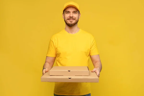 Porträt eines jungen Zustellers in gelber Uniform mit Pizzakartons auf gelbem Hintergrund. — Stockfoto