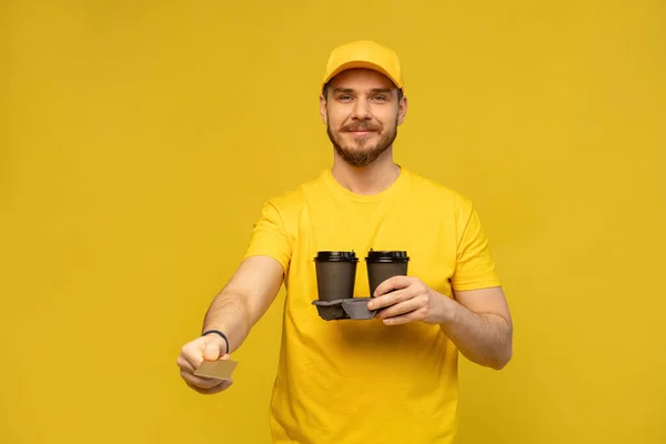 Porträt eines jungen Lieferanten in gelber Uniform mit Kaffee zum Mitnehmen auf gelbem Hintergrund. — Stockfoto