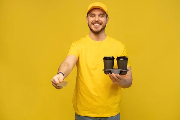 Porträt eines jungen Lieferanten in gelber Uniform mit Kaffee zum Mitnehmen auf gelbem Hintergrund. — Stockfoto